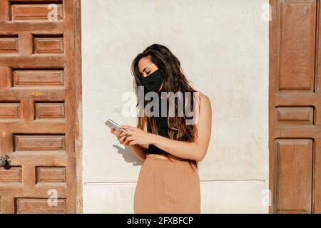 Female tourist wearing protective face mask while using mobile phone during sunny day Stock Photo