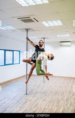 Male acrobat carrying female dancer while hanging on rod in dance studio Stock Photo