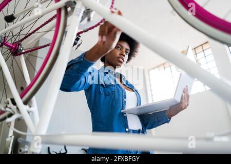 Young woman with laptop repairing bicycle at home Stock Photo