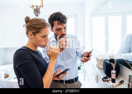Young couple using smart phone while brushing teeth in bathroom Stock Photo