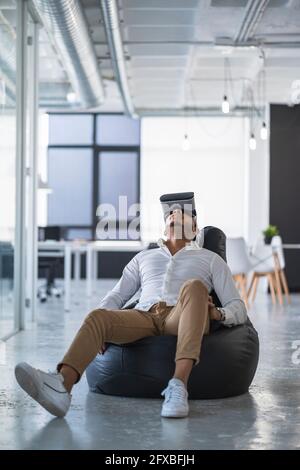Businessman using virtual reality simulator on bean bag at coworking office Stock Photo