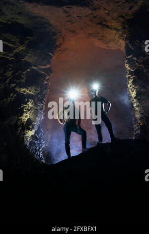 Male tourists exploring cave wearing illuminated headlamps Stock Photo