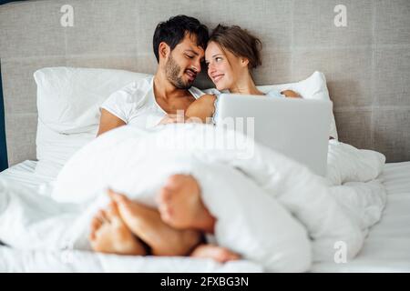 Smiling couple looking at each other while sitting on bed Stock Photo