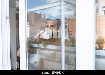 Man having coffee while looking through window seen through glass Stock Photo
