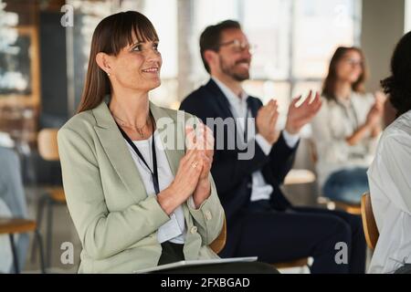 Businesswoman clapping hands with colleagues in conference centre Stock Photo