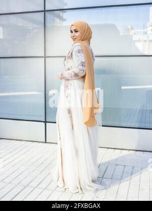 Young fashionable woman wearing hijab and dress standing on footpath Stock Photo