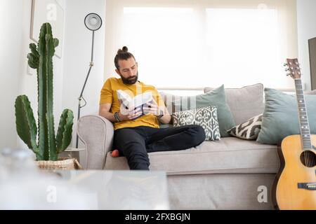 Handsome man reading book while sitting on sofa at home Stock Photo