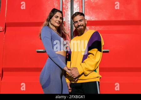 Smiling couple holding hands while standing in front of red container Stock Photo