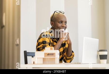 Smiling female architect with hands on chin looking away at home Stock Photo