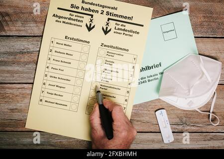 Hand checking ballot for federal elections by mail on table with protective mask and corona rapid test Stock Photo