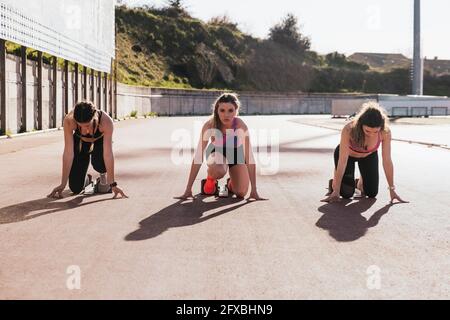 Sportswomen kneeling while preparing for race during sunny day Stock Photo