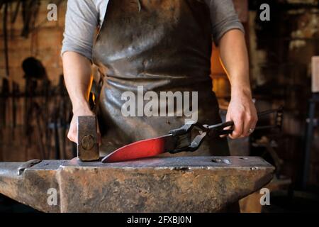 Blacksmith making knife of metal on anvil at blacksmith shop Stock Photo