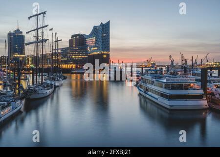 Germany, Hamburg, Boats in harbor and Elbe Philharmonic Hall illuminated at dusk