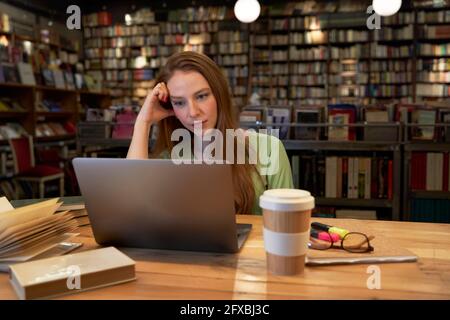 Young woman studying through laptop in library Stock Photo