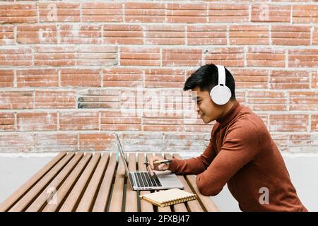Male entrepreneur with headphones talking during video call through laptop at cafeteria Stock Photo