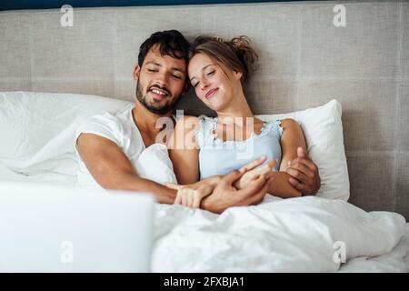 Young couple looking at laptop while sitting together on bed at home Stock Photo