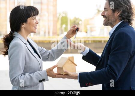 Mature professional smiling while taking house key and model through estate agent Stock Photo