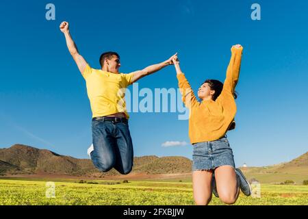 Carefree young couple jumping during sunny day Stock Photo