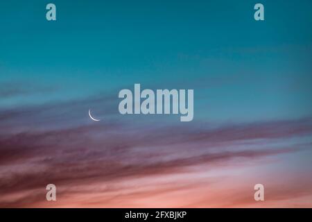 Crescent moon glowing against sky at dusk Stock Photo