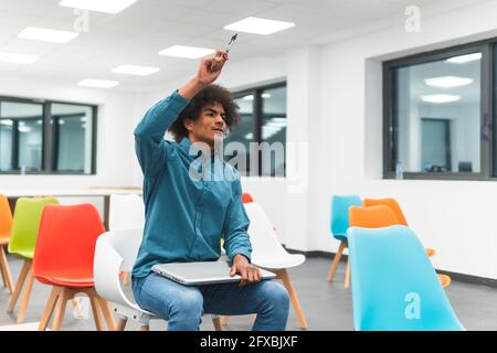 Businessman raising hand while sitting with laptop at education class room Stock Photo