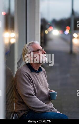 Thoughtful senior man sitting outside cafe at street Stock Photo