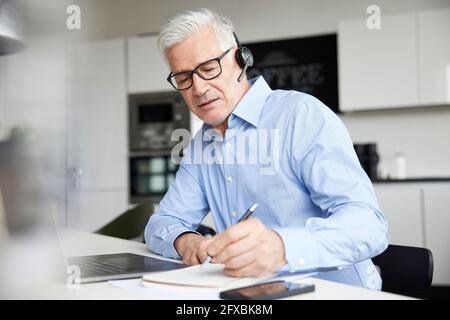 Male professional with wireless headset writing in book at office Stock Photo