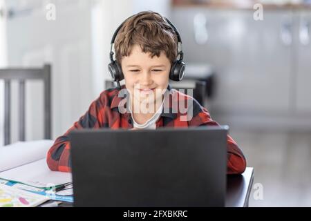 Smiling boy attending online classes through laptop while e-learning at home Stock Photo