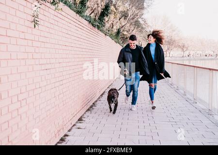 Couple enjoying while running with pet on footpath Stock Photo