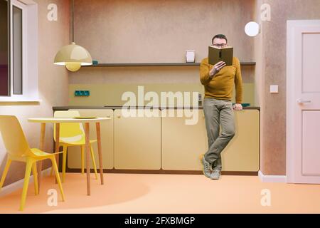 Mature man reading book while standing at home Stock Photo