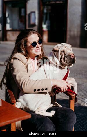 Woman wearing sunglasses sitting with dog during sunny day Stock Photo