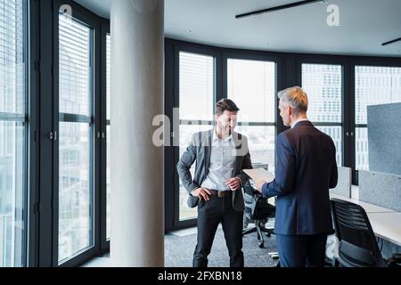 Male professional discussing over documents by architectural column in office Stock Photo