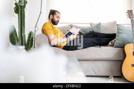 Man reading book while relaxing on sofa at home Stock Photo