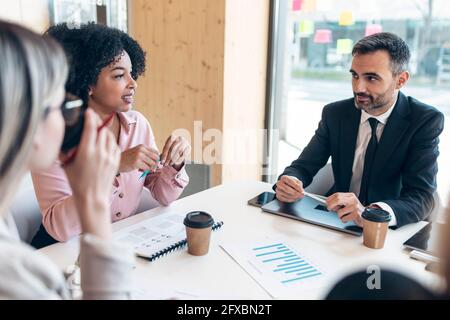 Businessman sitting with female professionals at conference table in office Stock Photo