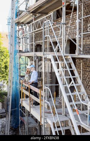 Female client showing construction to male architect while standing in balcony at site Stock Photo