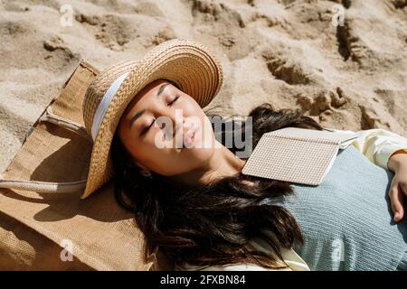 Woman with eyes closed lying on sand on sunny day Stock Photo