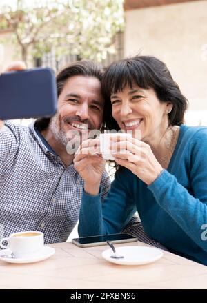 Smiling couple taking selfie on mobile phone while having coffee at terrace Stock Photo