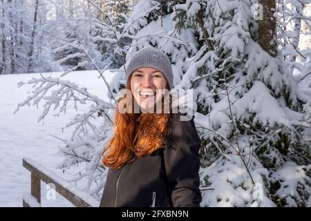 Happy woman with red hair in front of snow covered tree during winter Stock Photo