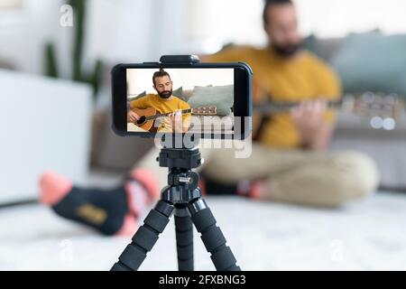 Handsome man filming while playing guitar at home Stock Photo