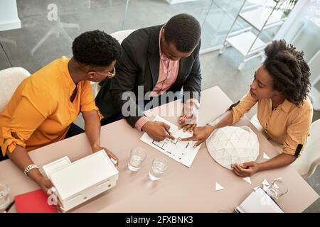 Female architect discussing over blueprint with colleagues in office Stock Photo