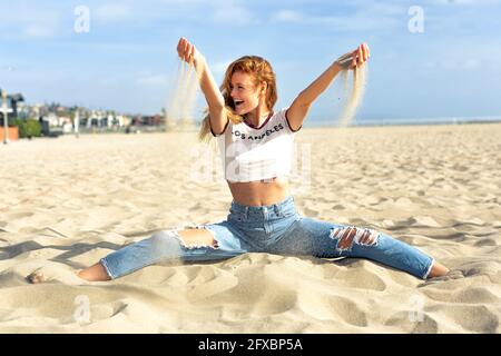 Carefree young woman playing with sand at beach on sunny day Stock Photo