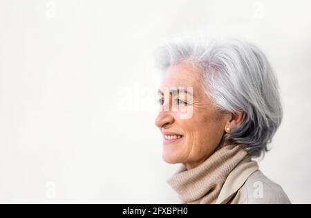 Smiling woman with gray hair contemplating by white wall Stock Photo