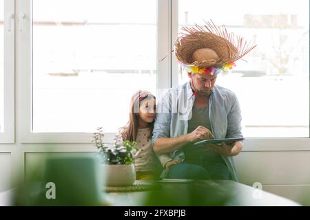 Man wearing straw hat using digital tablet while sitting by girl at home Stock Photo