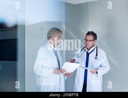 Senior male doctor discussing over reports with young healthcare worker in hospital Stock Photo