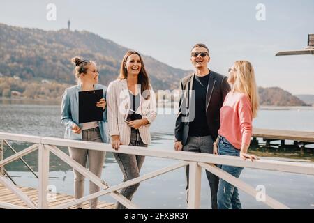 Cheerful female professionals with couple standing on jetty by lake Stock Photo