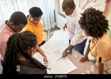 Female and male design professionals discussing over blueprints at coworking office Stock Photo
