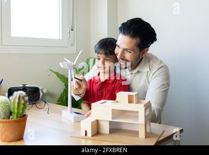 Smiling male architect showing turbine model to son at home office Stock Photo