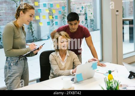 Female professional explaining business plan on laptop to coworkers in office Stock Photo