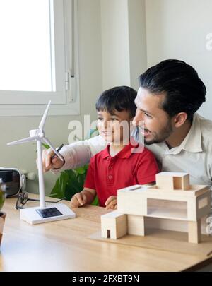 Smiling male architect discussing over wind turbine model with son at home Stock Photo