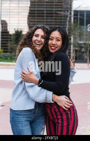 Smiling female friends hugging each other while standing outdoors Stock Photo
