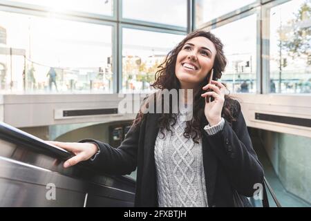 Smiling female professional looking up while moving up through escalator Stock Photo